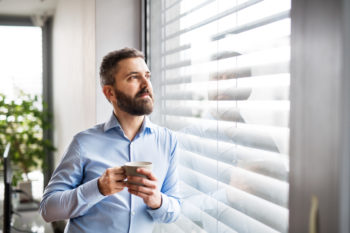 A man standing by the window, holding a cup of coffee and enjoying commercial hvac comfort.
