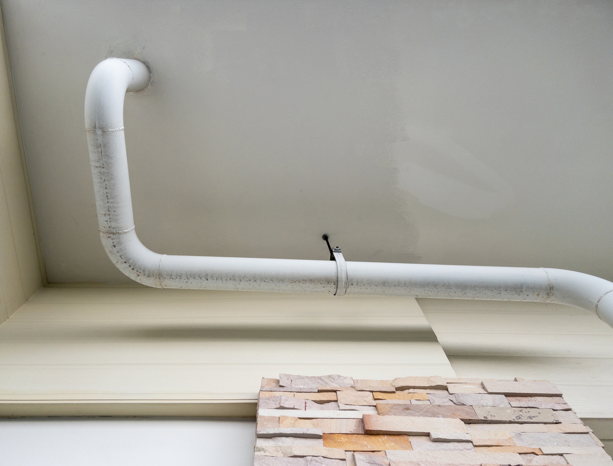 The white curve pipe for drainage of the air conditioner system is hanging on the ceiling of the office building. 